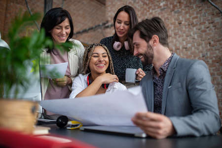 Cheerful young and old businesspeople sitting and working at desk in office, cooperation concept.の写真素材