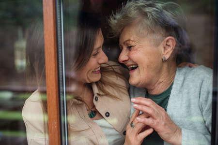 Close-up portrait of happy senior mother with adult daughter indoors at home, hugging and laughing.の写真素材