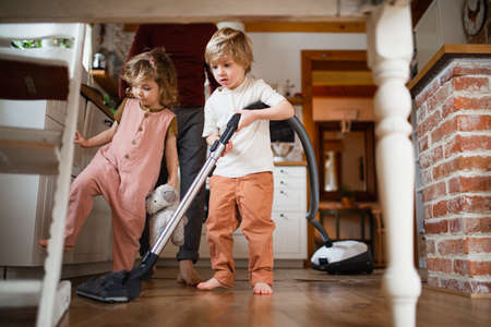 Unrecognizable father with two small children hoovering indoors at home, daily chores concept.の写真素材