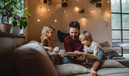 Mature father with two small children resting indoors at home, looking at photo album.の写真素材
