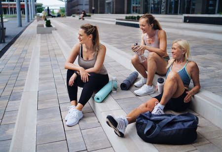 Group of young and old women sitting after exercise outdoors in city, talking.の写真素材