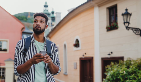 Young man outdoors on trip in town, using online map on smartphone.