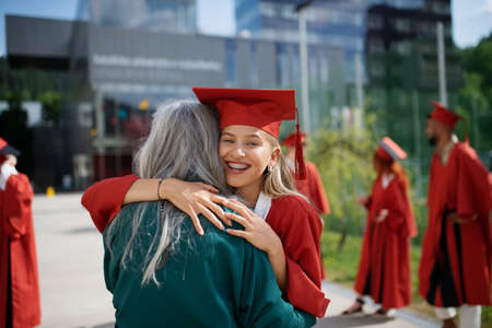 Portrait of cheerful university student hugging mother outdoors, graduation concept.の写真素材