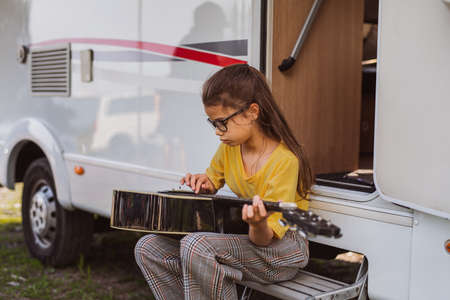 Small girl with guitar playing by caravan, family holiday trip.の写真素材