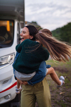 Mother with daughter having fun by car outdoors in campsite at dusk, caravan family holiday trip.の写真素材