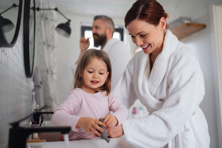 Father and mother with small daughter washing indoors in bathroom in the evening or morning.の写真素材