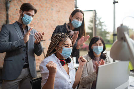 Young and old businesspeople feeling joyful at desk in office, cooperation and coronavirus concept.の写真素材