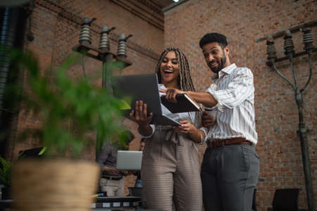 Cheerful young businesspeople with laptop working in office, cooperation concept.