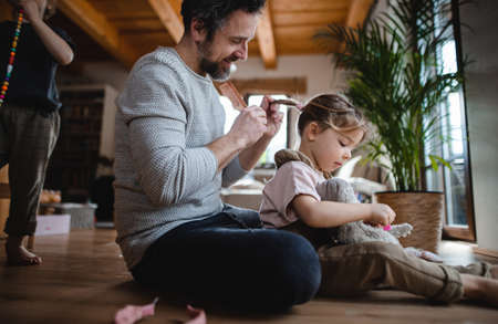 Mature father with small son and daugther resting indoors at home, playing and combing hair.の写真素材