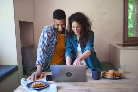 Happy couple with laptop sitting, resting and talking indoors in a tree house, weekend away and...