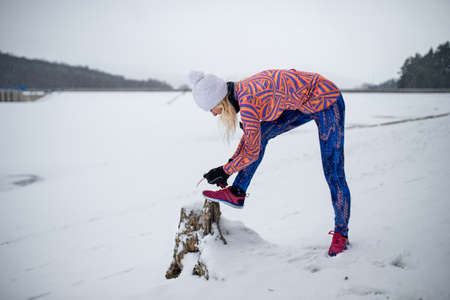 Active senior woman outdoors in snowy winter, tying shoelaces.の写真素材