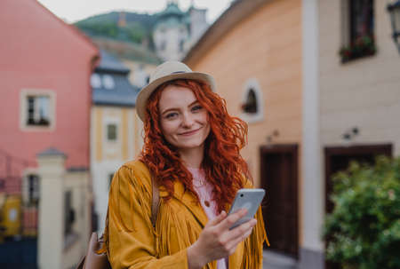 Young woman tourist with smartphone outdoors on trip in town, looking at camera.の写真素材