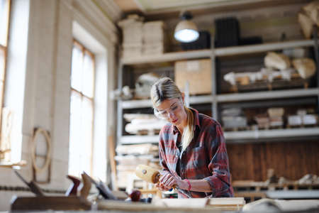 Portrait of female carpenter with goggles working on her product. Small business concept.