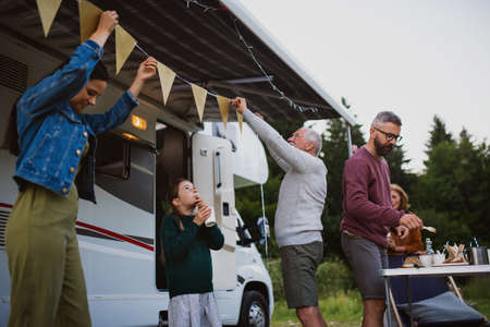 Multi-generation family preparing party by car outdoors in campsite, caravan holiday trip.の写真素材