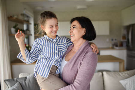 Happy small girl with senior grandmother indoors at home having fun.