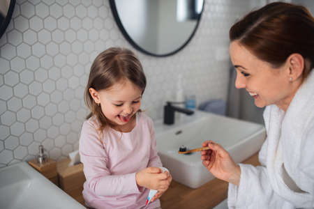 Mother with small daughter brushing teeth indoors in bathroom in the evening or morning.の写真素材