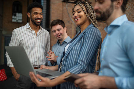Cheerful young businesspeople with laptop working in office, social inclusion and cooperation...