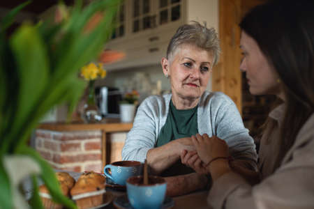 Sad senior mother having tea with adult daughter indoors at home, talking.