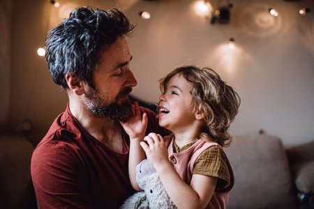 Mature father with small daughter standing indoors at home, holding and hugging.の写真素材