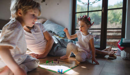 Unrecognizable father with two small children resting indoors at home, playing board game.