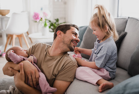 Happy young man taking care of his newborn baby and little daughter indoors at home, paternity leave.の写真素材