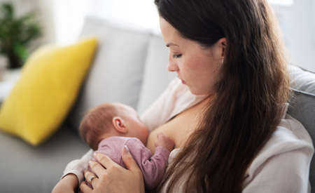 Young mother breastfeeding her newborn baby girl indoors at home, maternity leave.の写真素材