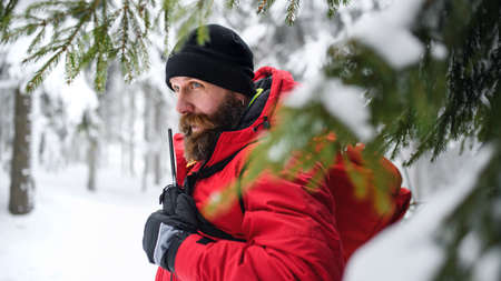 Paramedic man from mountain rescue service with walkie talkie outdoors in winter in forest.