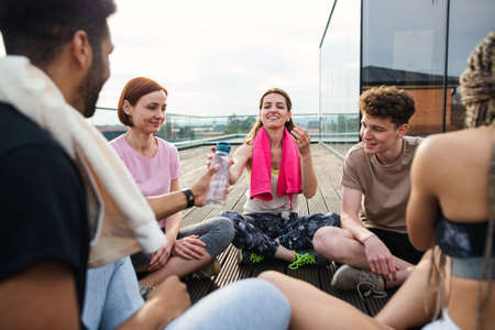 Group of young people talking and sitting in circle after exercise outdoors on terrace, sport and healthy lifestyle concept.の写真素材
