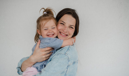 Portrait of happy young mother with her little daughter hugging and looking at camera, on white background.の写真素材
