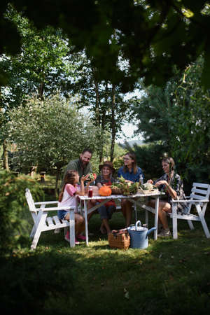 Family of farmers sitting by the table and looking at their harvest outdoors at community farm.の写真素材