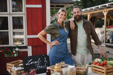 Mature couple farmers selling homegrown products at community farmers market, looking at camera.の写真素材