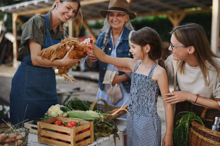 Little girl with mother stroking hen outdoors at community farmers market.の写真素材