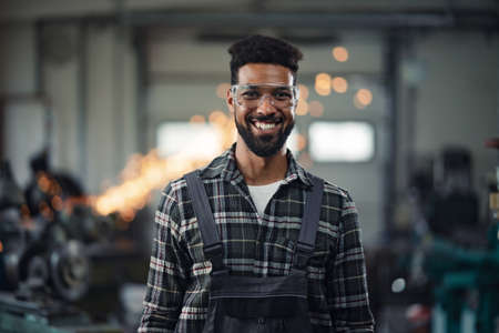 Portrait of young industrial man working indoors in metal workshop, looking at camera.の写真素材