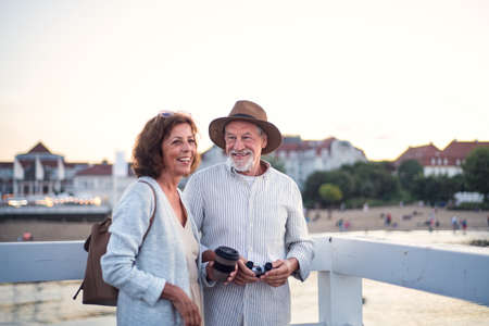 Happy senior couple hugging outdoors on pier by sea, smiling.の写真素材