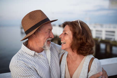 Happy senior couple hugging outdoors on pier by sea, looking at each other.の写真素材