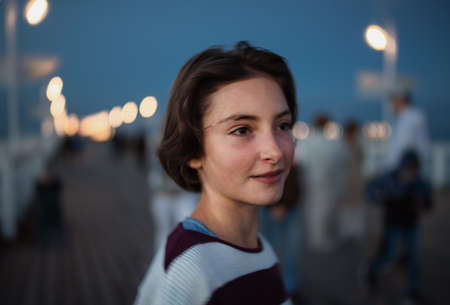 Portrait of preteen girl looking aside outdoors on pier by sea at dusk, holiday concept.の写真素材