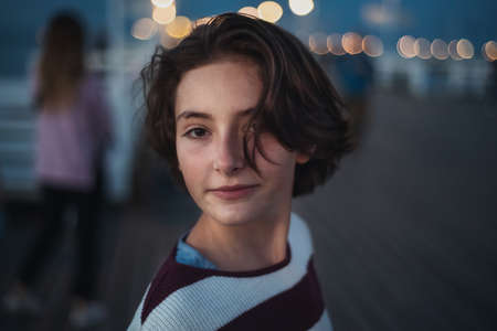 Portrait of preteen girl looking at camera outdoors on pier by sea at dusk, holiday concept.の写真素材