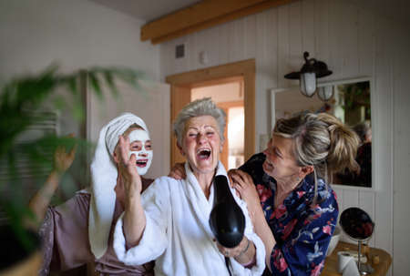 Happy senior women friends in bathrobes having fun indoors at home, selfcare concept.