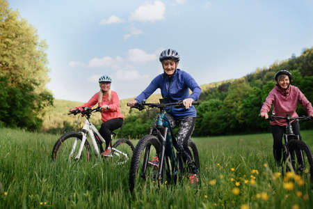 Low angle view of happy active senior women friends cycling together outdoors in nature.の写真素材