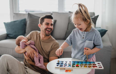 Happy young man taking care of his newborn baby and little daughter indoors at home, paternity leave.の写真素材