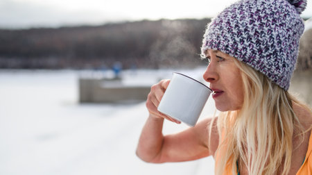 Portrait of active senior woman in sports clothes drinking tea outdoors in winter, cold therapy concept. Copy space.の写真素材