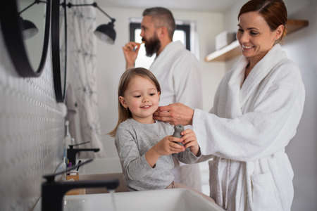 Father and mother with small daughter washing indoors in bathroom in the evening or morning.の写真素材