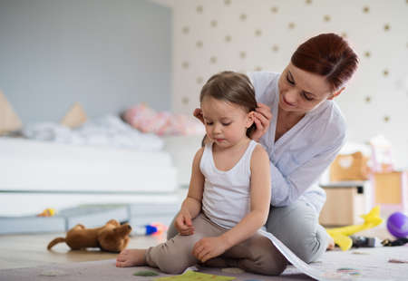 Happy mother with small daughter playing indoors in bedroom, laughing.の写真素材