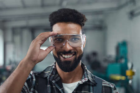 Portrait of happy young industrial man working indoors in metal workshop, looking at camera.の写真素材