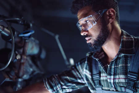 Close up of young concentrated african american industrial man working on cutter indoors in metal workshop.の写真素材