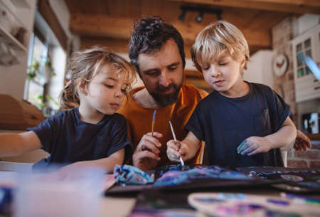 Mature father with two small children resting indoors at home, painting pictures.の写真素材