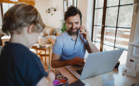 Mid adult father with small son working indoors at home, painting pictures and home office concept.の写真素材