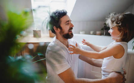Mature father with small daughter indoors at home, getting ready for a bath.の写真素材