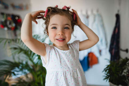 Portrait of small girl with hair curlers indoors at home, looking at camera.の写真素材