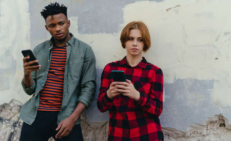 Young biracial couple addicted to smartphones outdoors in town, social media conceptの写真素材